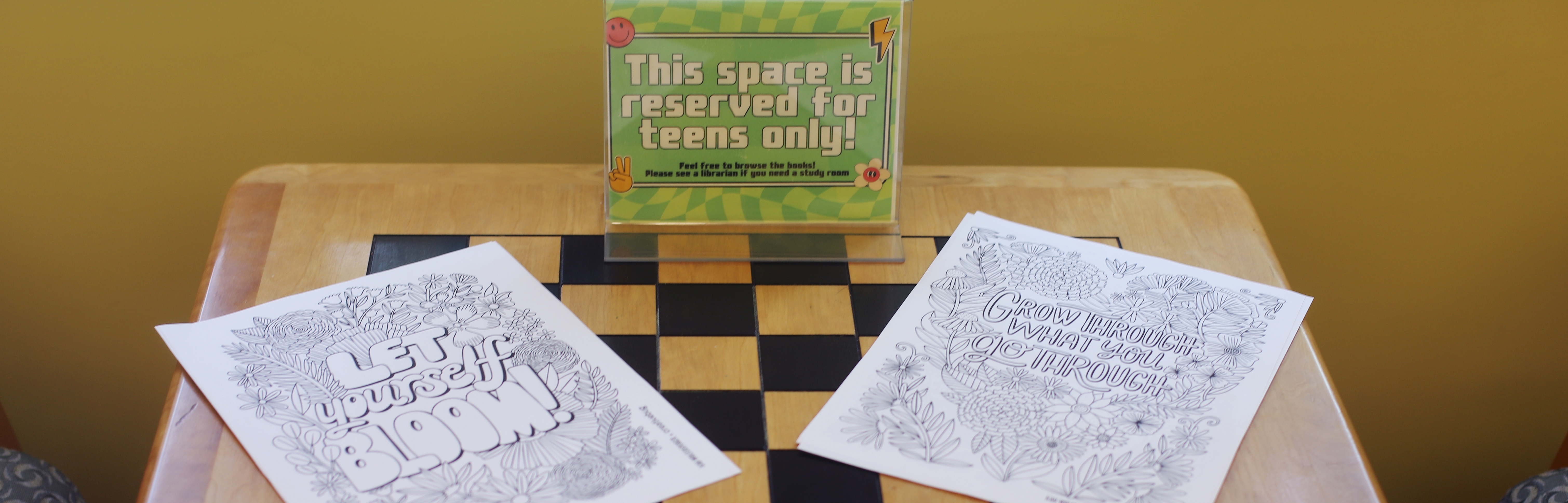 sign saying "this space is reserved for teens only" with coloring pages on a checker print table